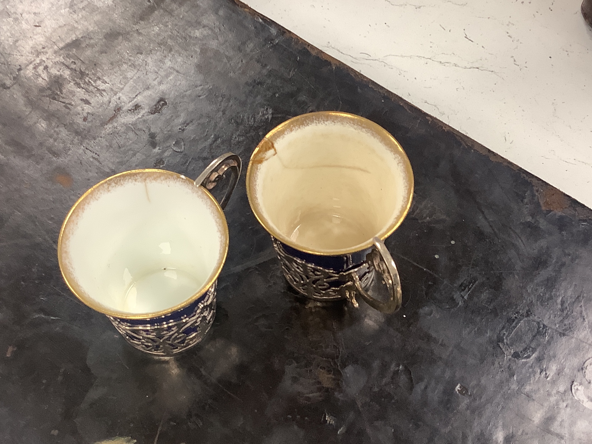 A set of six blue and gilt edged coffee cups and saucers, the cups with pierced silver holders, London, 1919, together with a set of 6 coffee spoons, triffid end terminals, Sheffield, 1925, cased